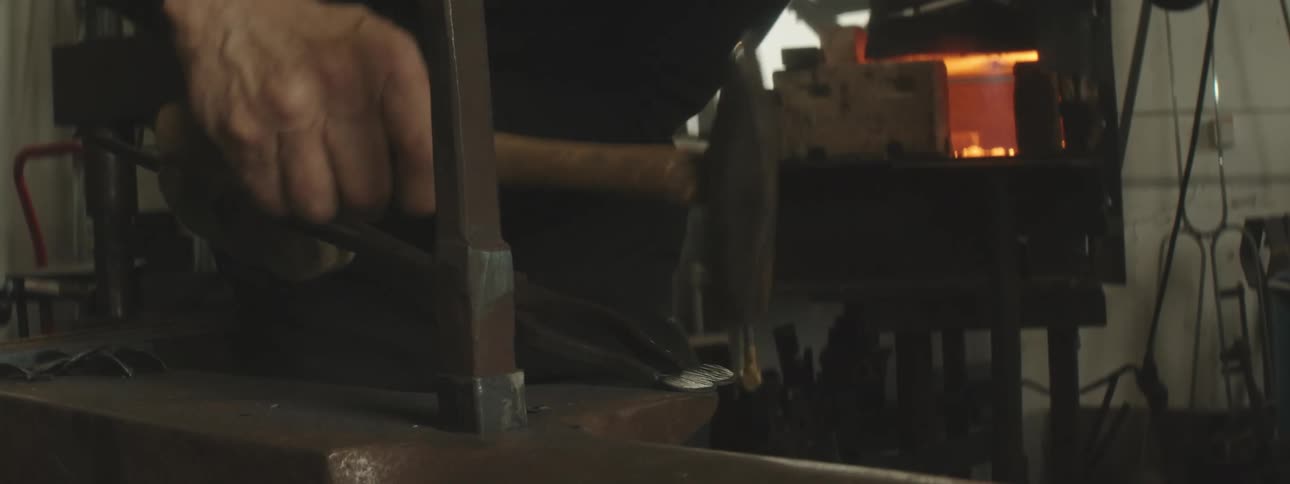 Closeup of a mans hands hammering a metal rod and then placing it in a furnace