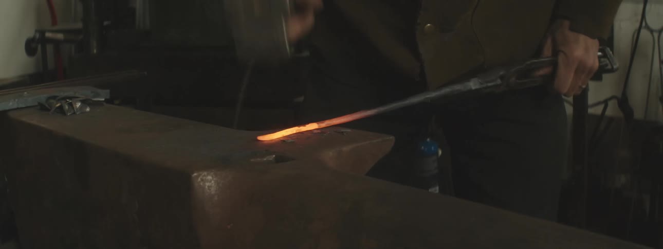 A person is hammering a hot metal rod on an anvil in a workshop