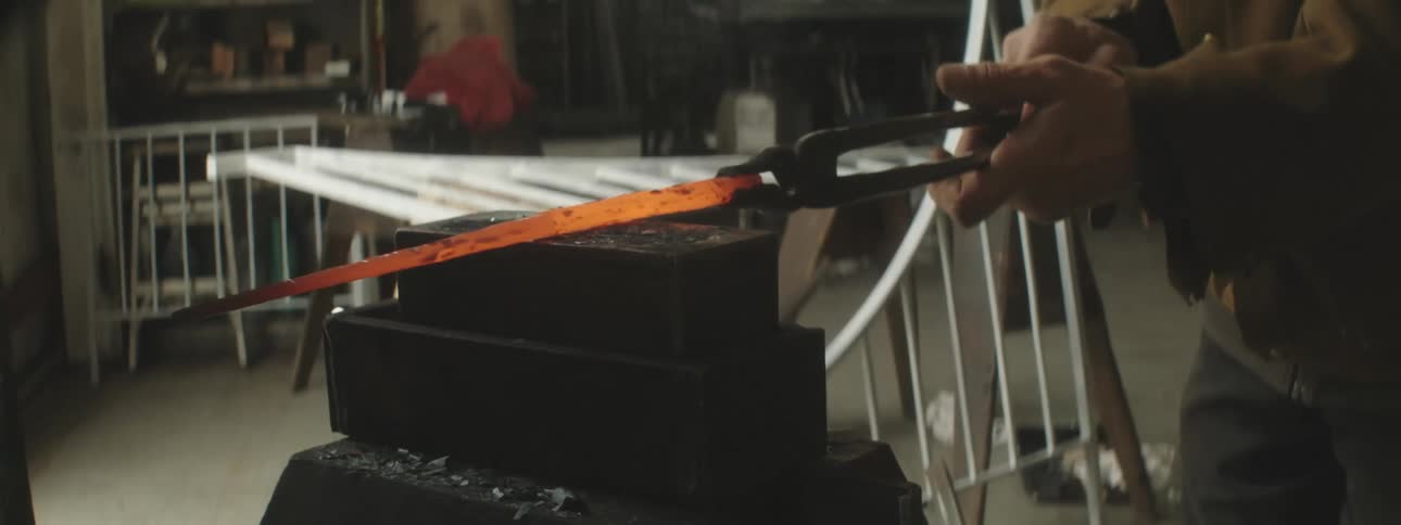 An employee uses a press to shape a piece of hot metal