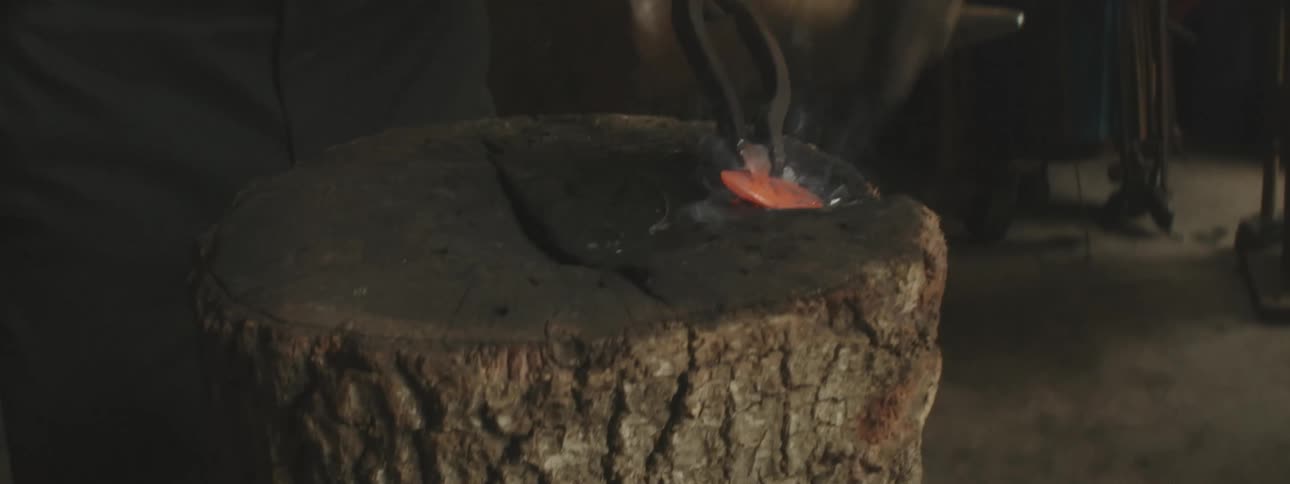 A person hitting a hot steel with a hammer on top a wood