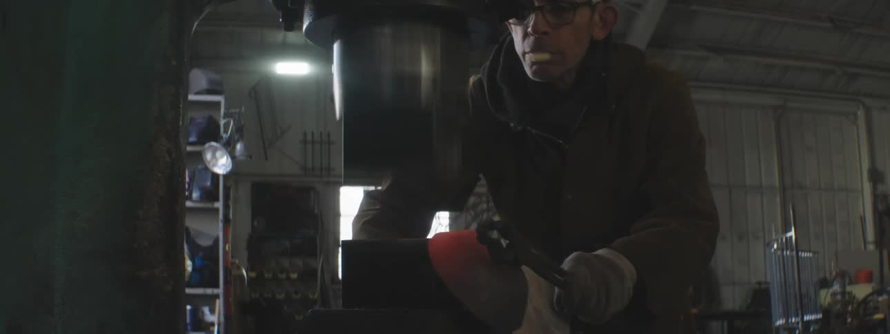 A man is using a machine to hammer hot metal