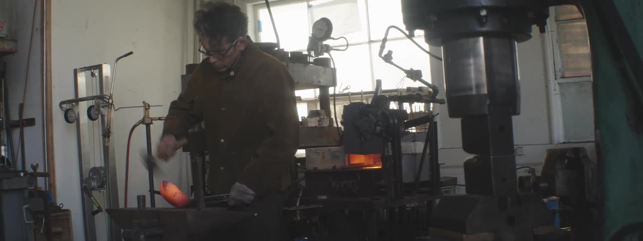 A man is hammering hot metal in his shop