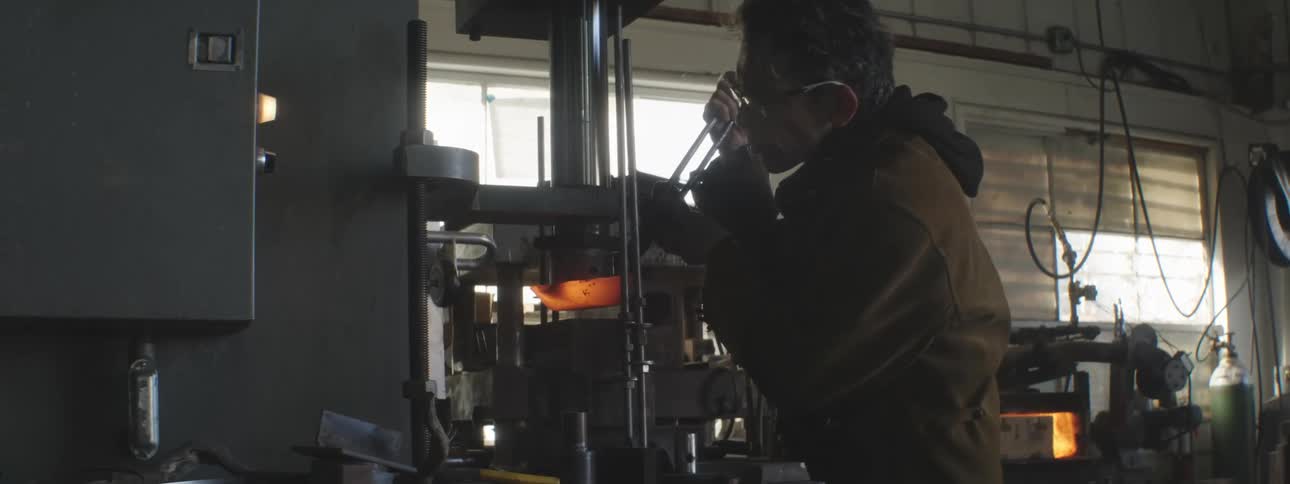 A man uses a press to shape a piece of molten hot metal