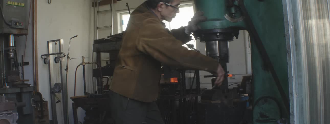 A blacksmith uses a large machine to hammer hot metal