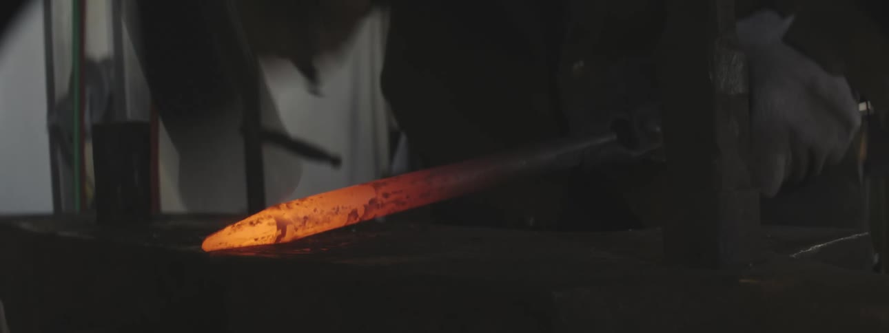 Hands of a person hammering and shaping the tip of a hot iron