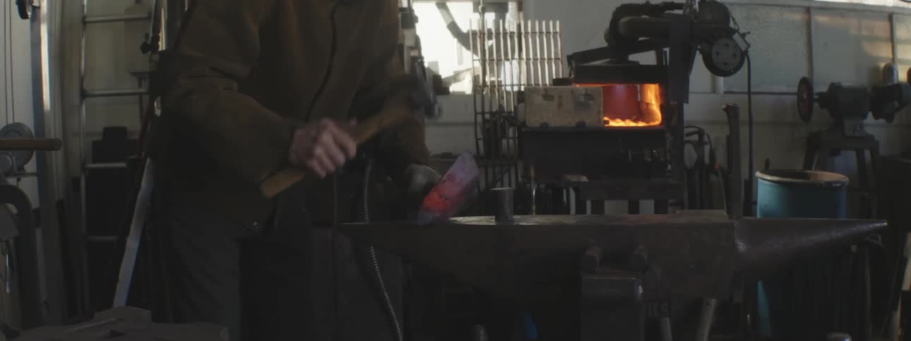 A man is hammering hot metal near the forge