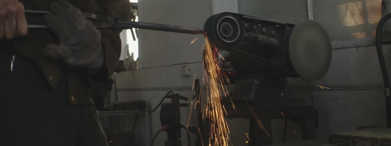 Hands of a man turning on a machine and shaping an iron rod causing sparks to come out