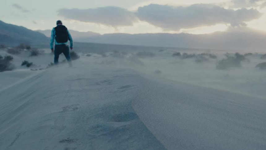 Man wearing a backpack walks across a sand storm
