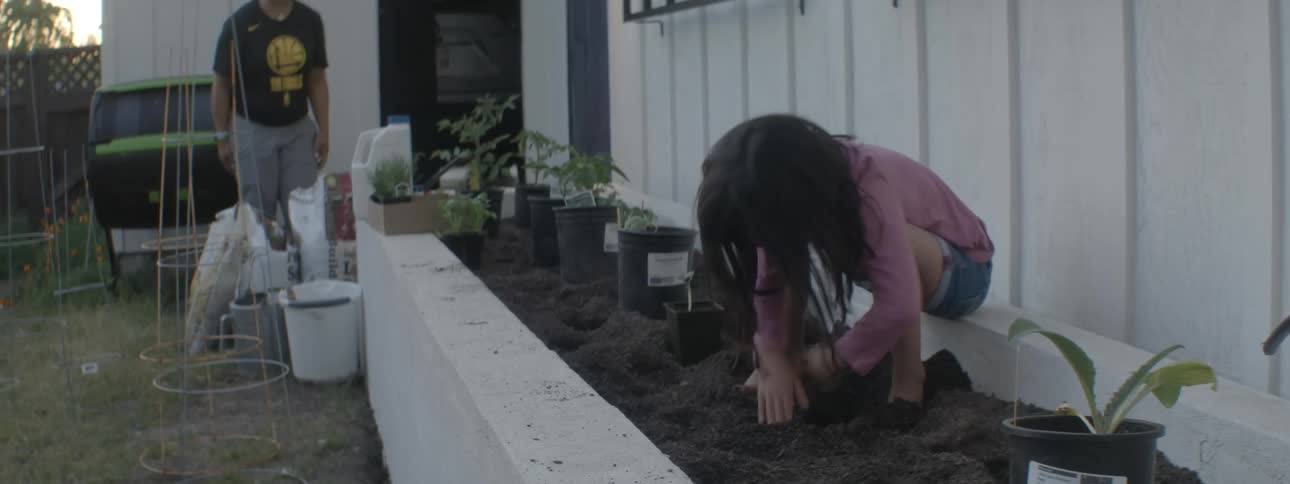Little girl on the ground next to a potted plant burying her foot