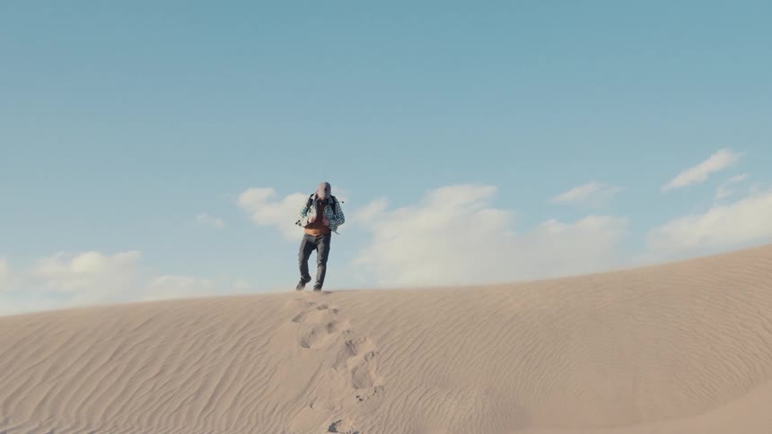 A man puts on a backpack and walks down Mesquite dunes