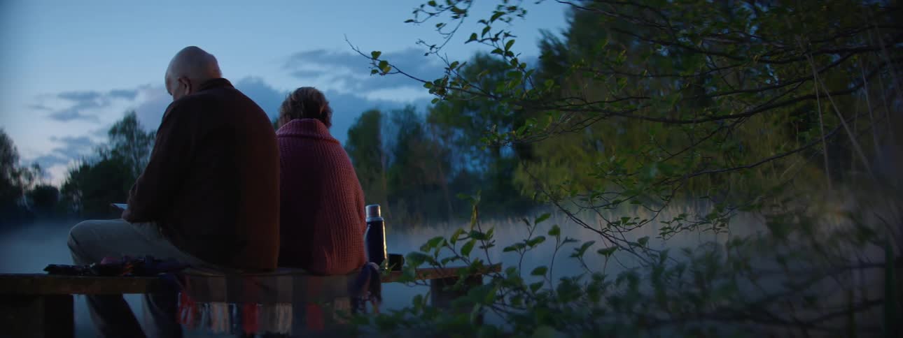 An elderly couple sitting on a park bench by a foggy lake