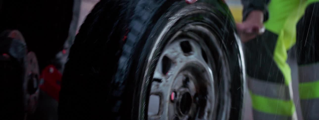 A mechanic changing a car wheel while it rains
