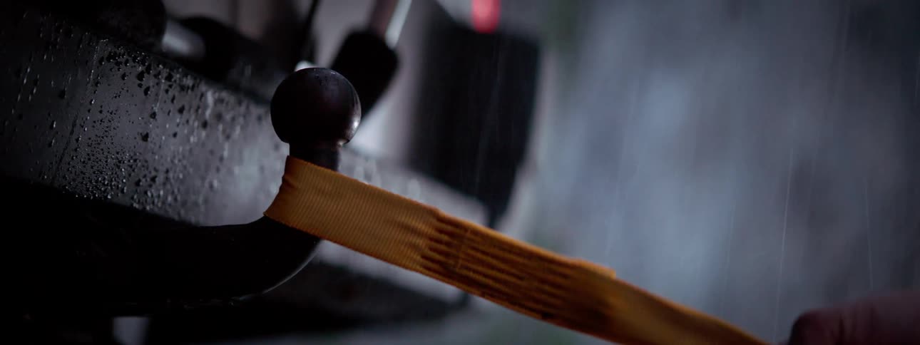 In the rain a hand hooks an orange strap onto a trailer hook then removes it