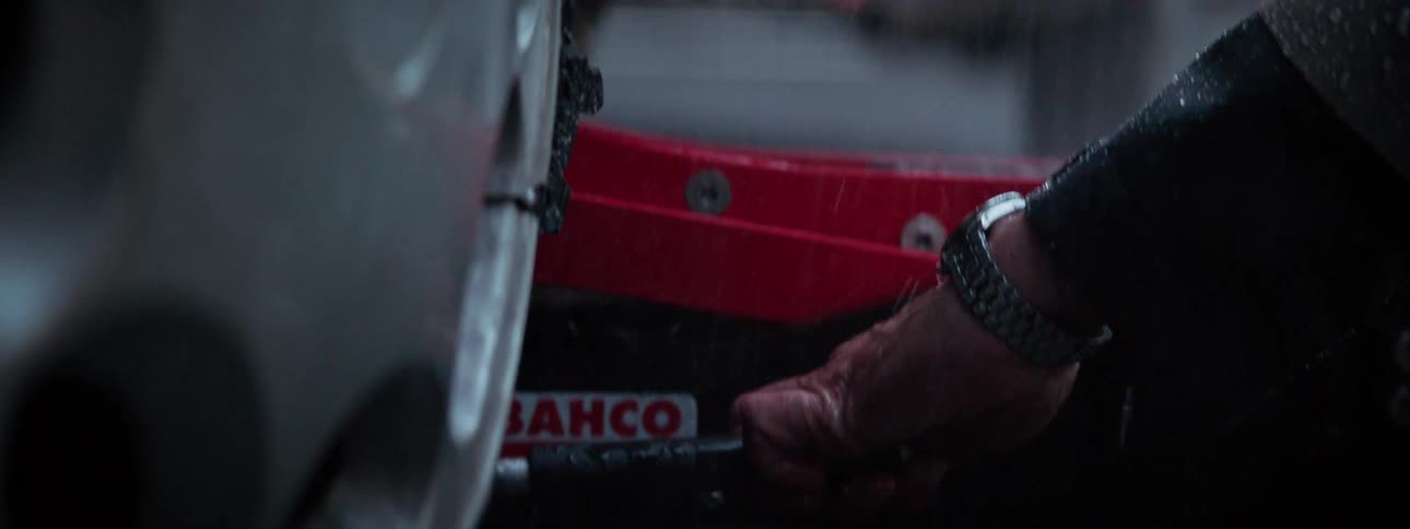 Person wheels a jack under a car body near wheel during the rain