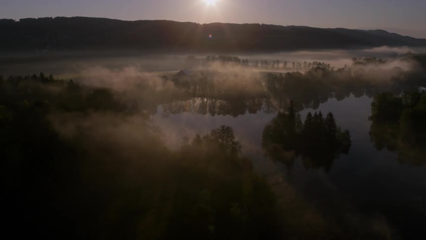 An aerial view captures a fogcovered field with a serene lake on a misty morning