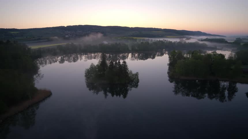 Beautiful natural landscape of a lake surrounded by vegetation with the sunrise and a purple and reddish sky