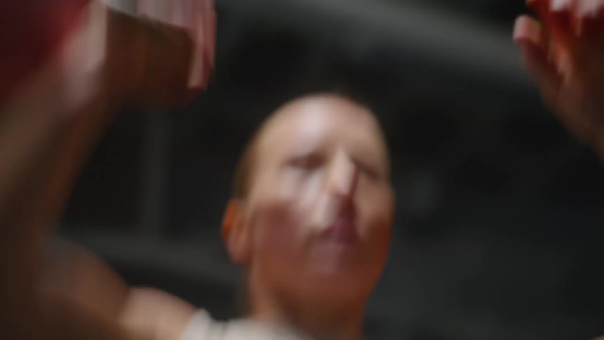A muscular woman raises a kettle bell weight over her head many times