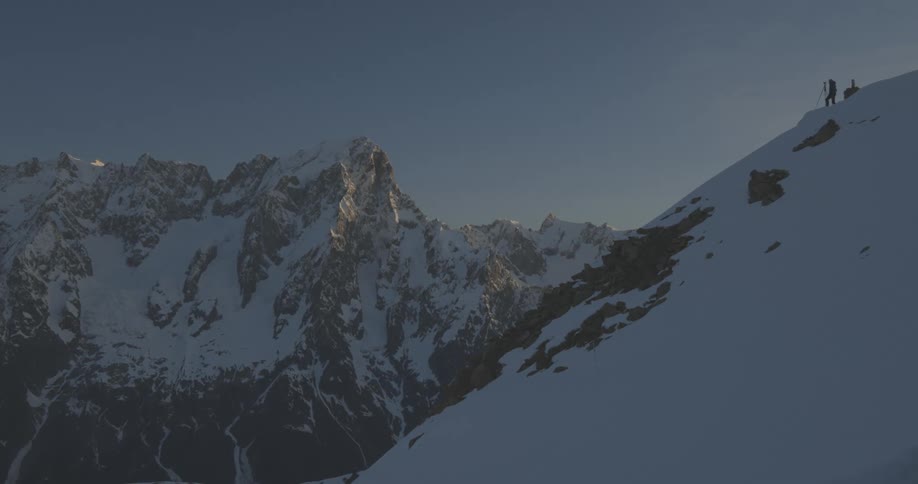 A person stands atop a snowcovered slope of a large mountain