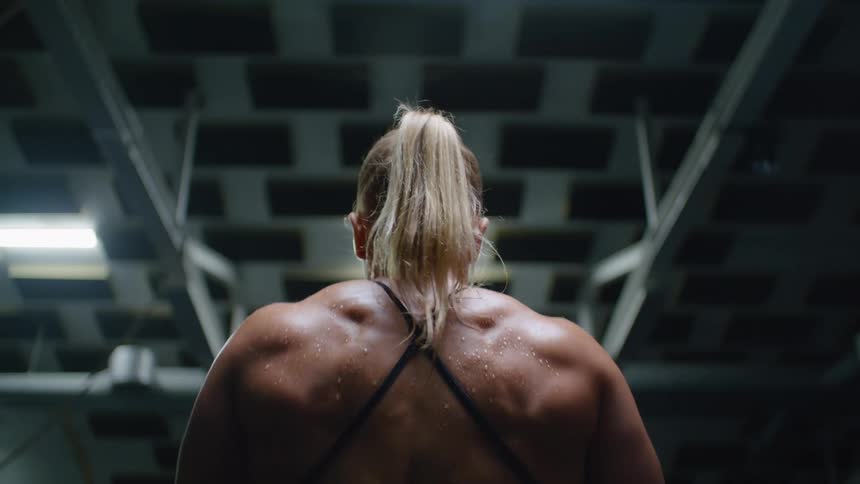 A very muscular woman flexes and rolls her shoulders in a gym