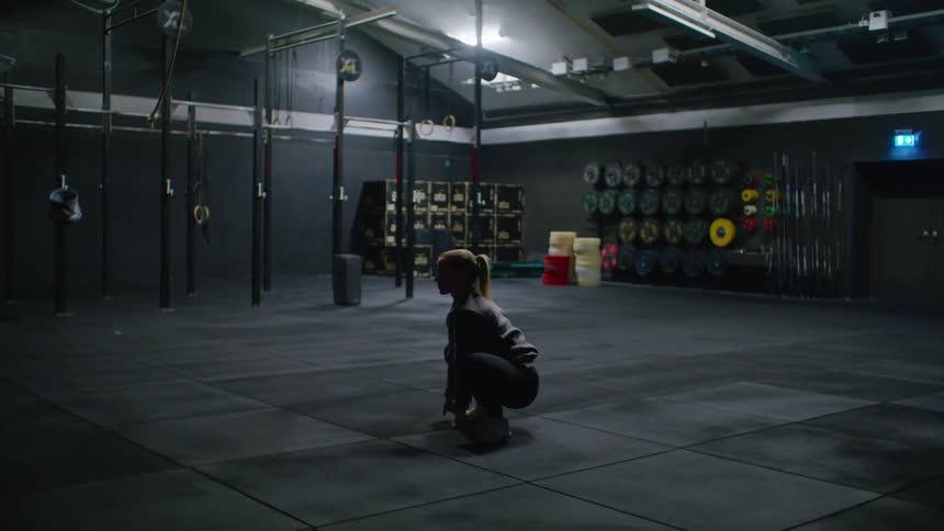 Blonde woman exercises while crouching in gym