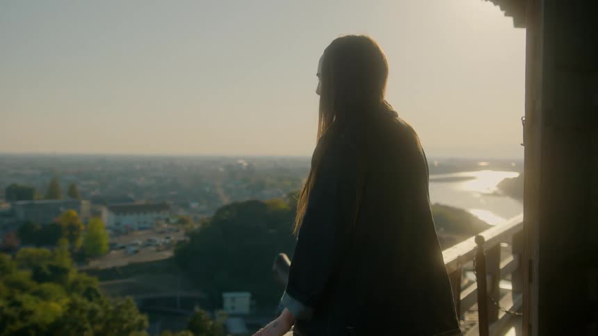A woman stands on a balcony overlooking buildings