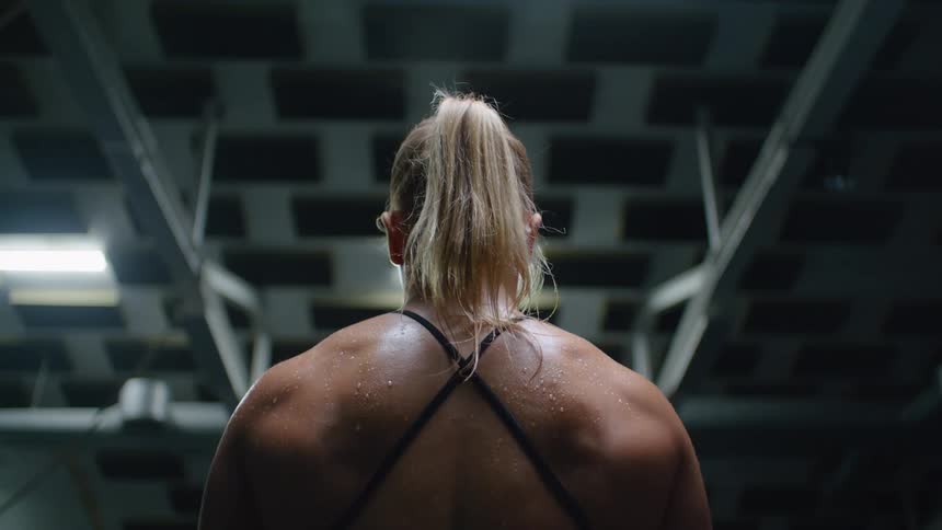A female bodybuilder with her shoulders covered in sweat breathes heavily