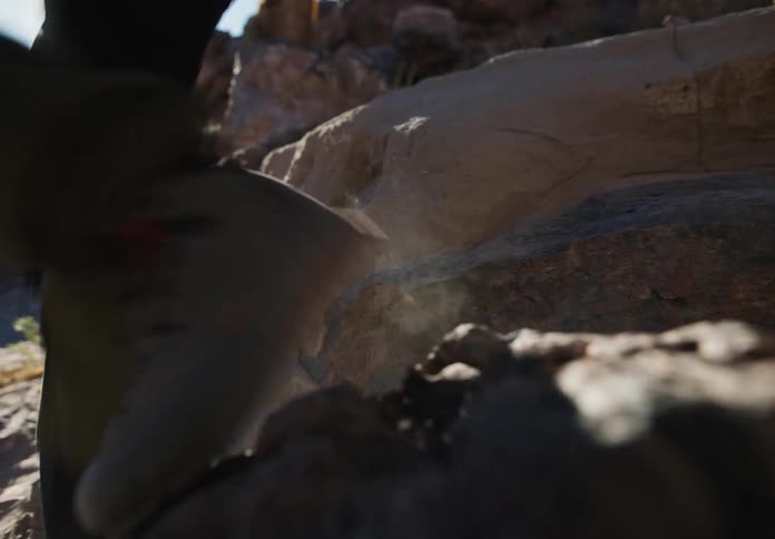 A hiker dressed in dark green pants and sturdy boots makes their way down the slope of a mountain