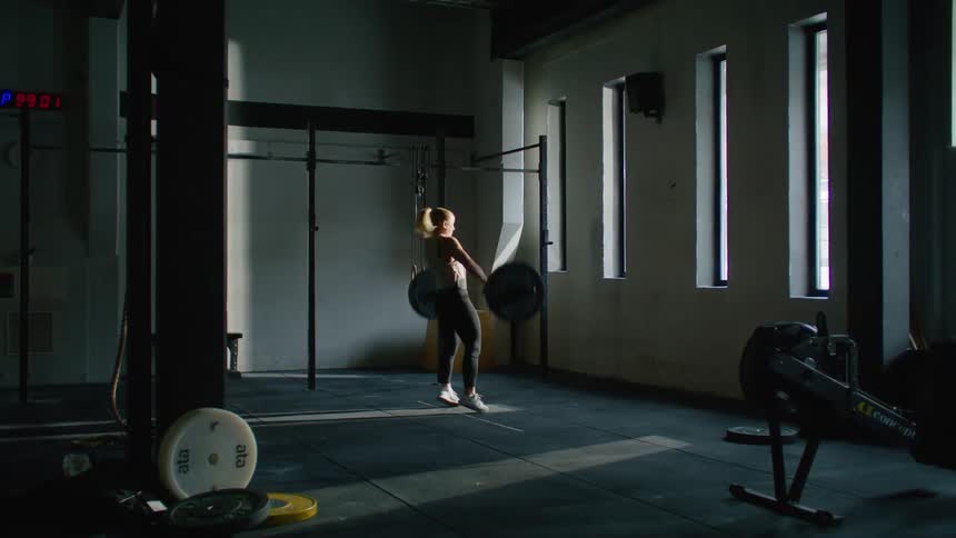 A woman picks up a weight from the floor and lifts it over her head