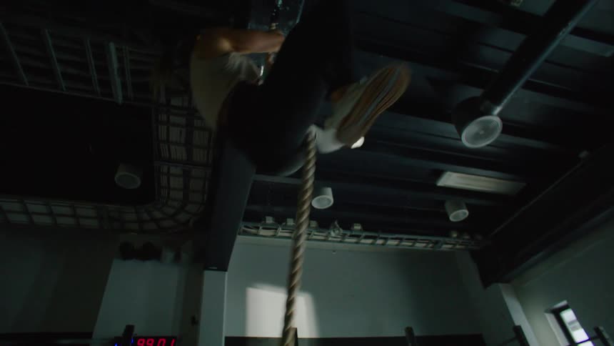 A blonde woman jumps on a rope and climbs it exercising