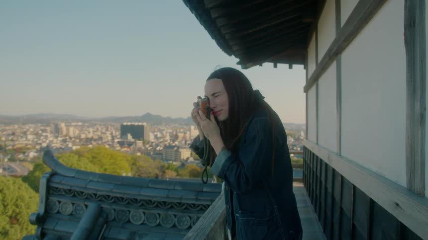 Woman looks through a camera on her balcony with a metropolis in the distance