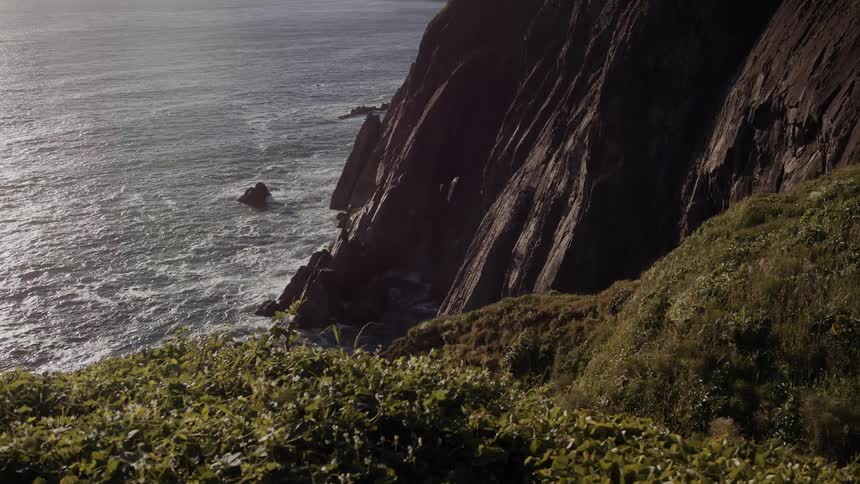 Waves flow past rock outcroppings and onto base of stone cliff