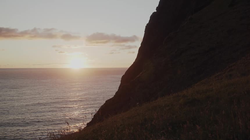The sun shines over the ocean with the side of a cliff in view