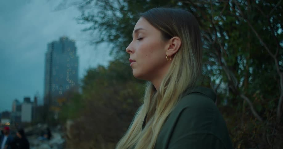 A woman on a city park with her eyes closed taking deep breaths