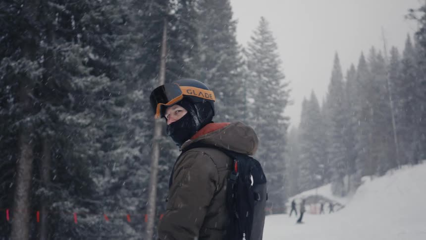 Man on facemask with backpack snowboarding in the snow at midday