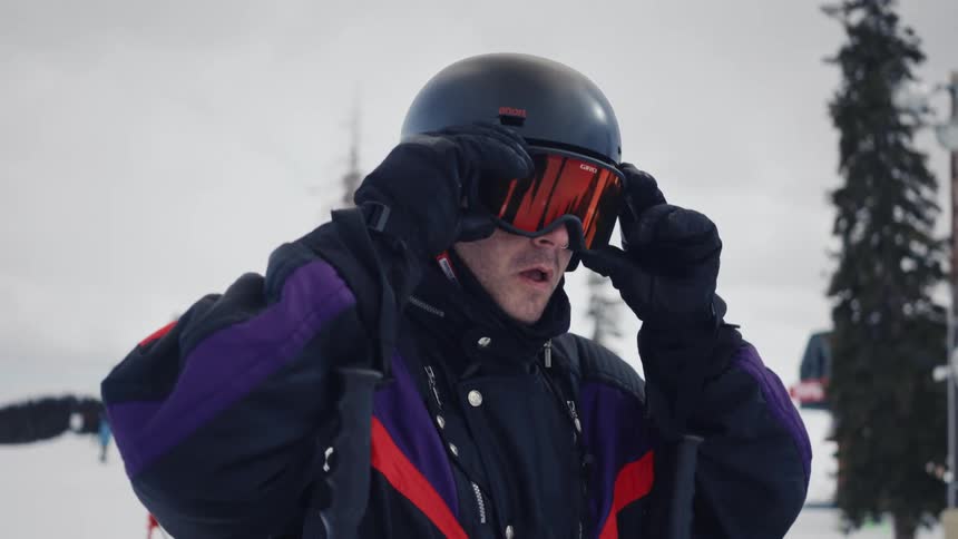 Man on a snow mountain in a park putting on his goggles