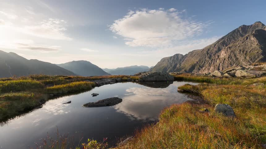 Beautiful landscape of a small lake with rocks and mountains around and clouds passing by in a blue sky