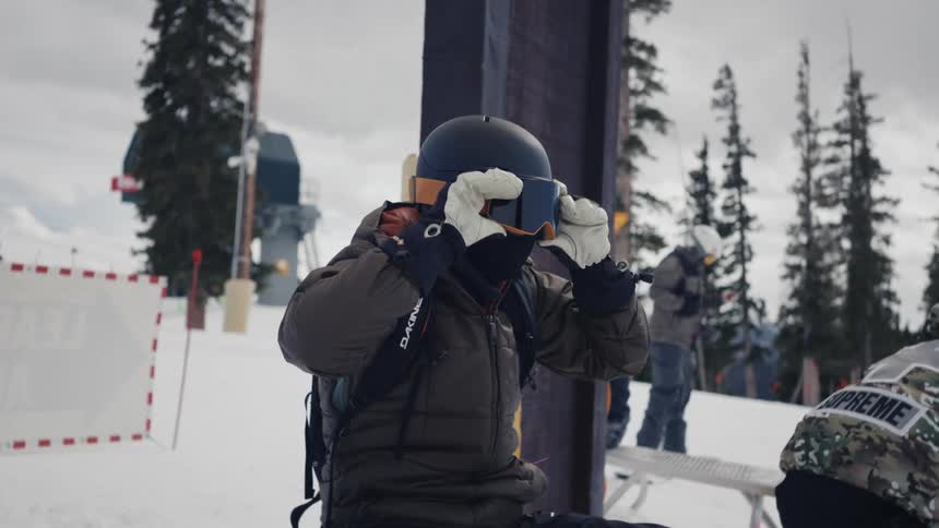 Man with ski equipment putting on his goggles while sitting on a bench on a snowcovered mountain