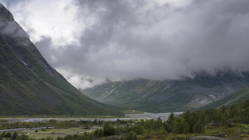 Aerial of a river between mountains and forests on a cloudy day