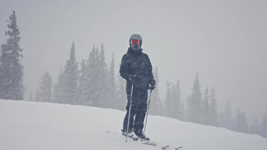 Person standing still with ski equipment on a snowing day in the mountain