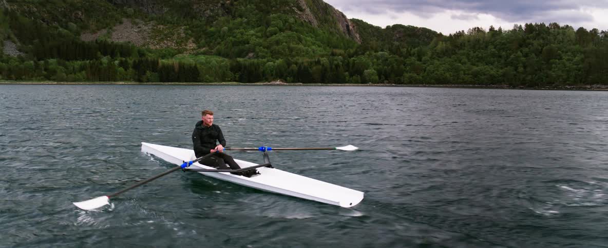 A man rows a boat toward lush forest out on the open water in a majestic landscape