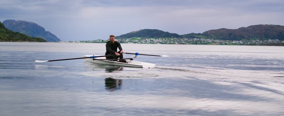 A man rows a boat off of a coast