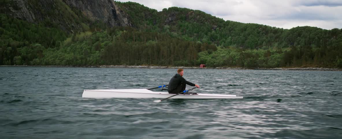 Man rows in the sea surrounded by rugged mountains and forests
