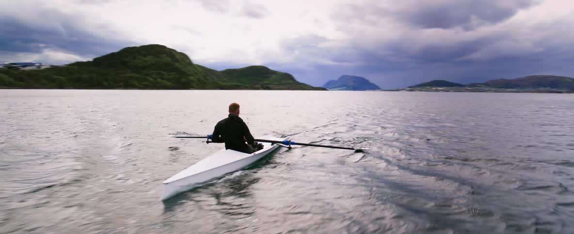 360 orbit shot of a man rowing a boat at dusk as he glides across the water