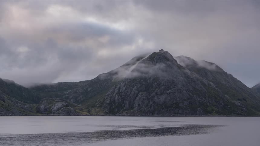 A mountain view sitting close to a river as the atmosphere is covered in mist