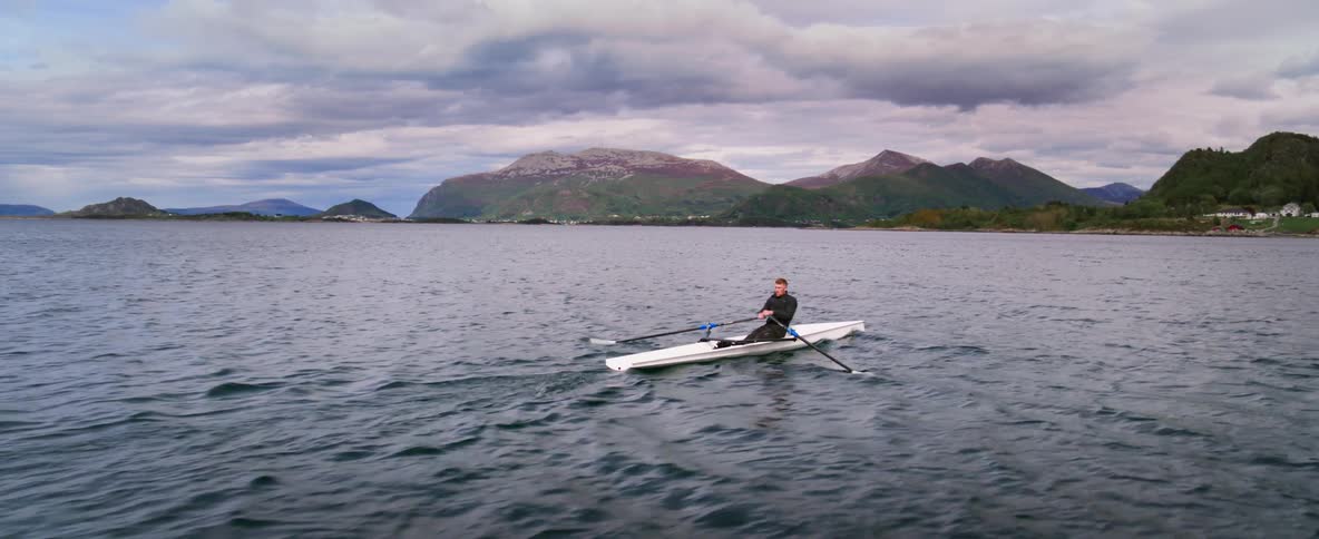 Fast motion tracking alongside an athlete as he glides along the water at dusk
