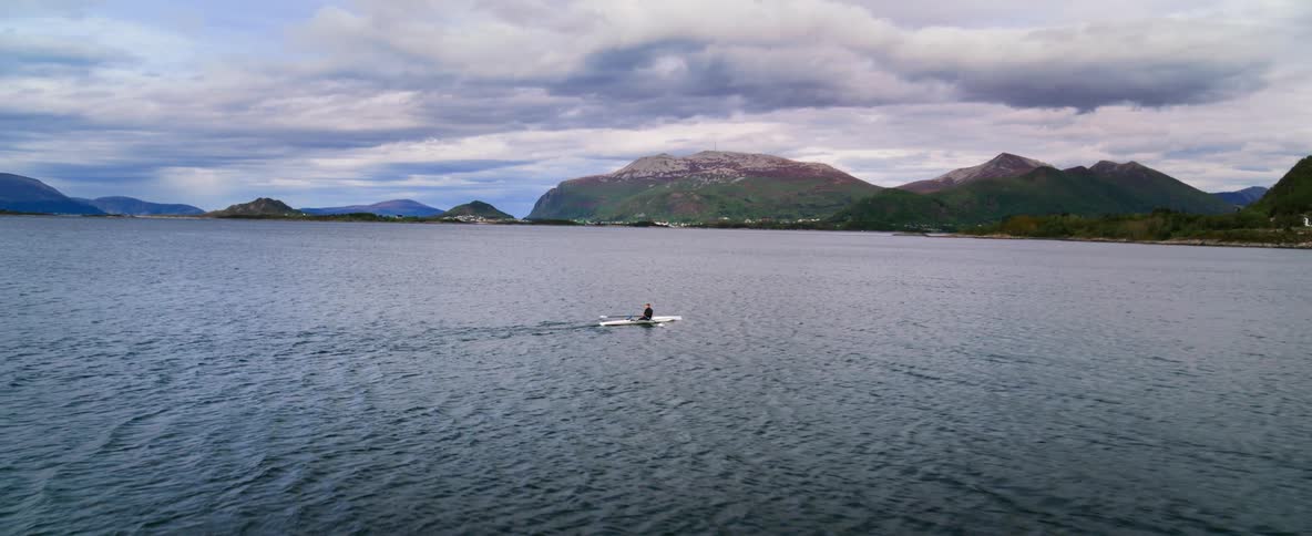 Aerial shot of a solo rower out on the open water at dusk in an epic landscape