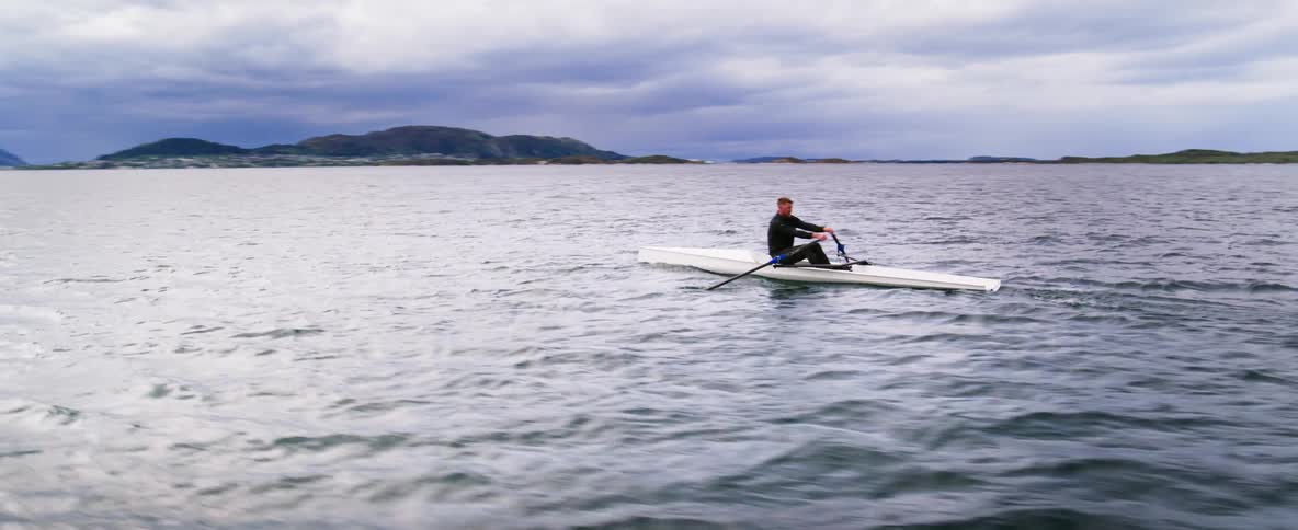 360 orbit shot of a man in a boat rowing across waves on an overcast day