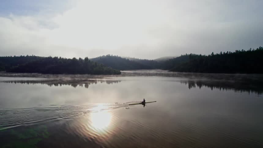 Solo rower in the soft light of the early morning on a peaceful lake with the sun reflecting on water