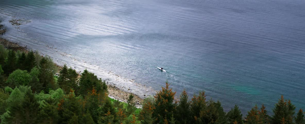 Aerial landscape of a peninsula with the blue sea and forests and a man in a boat