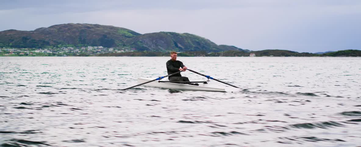 Intimate shot of a determined athlete rowing in the early moments of dawn surrounded by nature